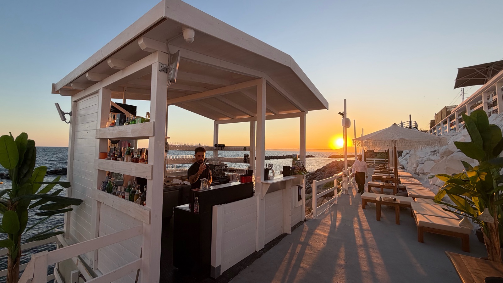 Il chiosco bar bianco del lido al tramonto, con il barman al bancone